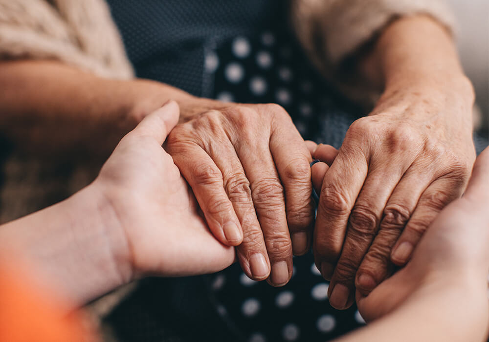Close up of a young person holding a senior woman's hands