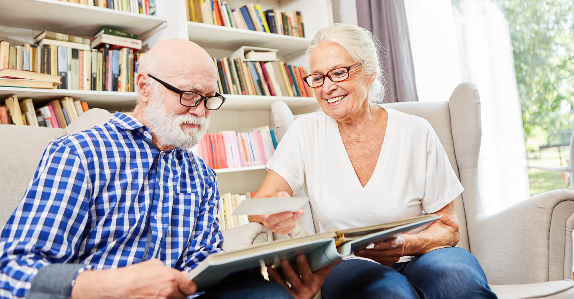 Senior couple sits on couch and looks through scrapbook